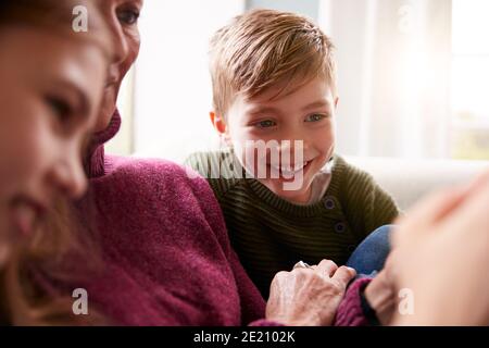 Enkelkinder Auf Sofa Zu Hause Großmutter Zeigen, Wie Man Benutzt Mobiltelefon Stockfoto