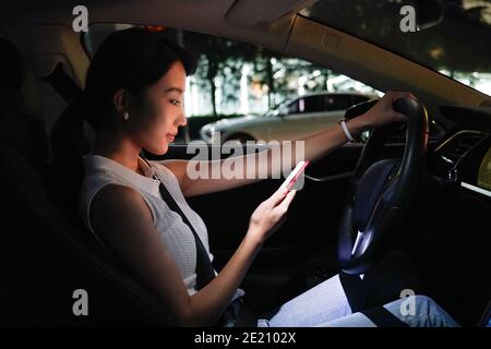 Junge Frau, die im Auto auf der Zelle des Fahrers sitzt Telefonnutzung Stockfoto