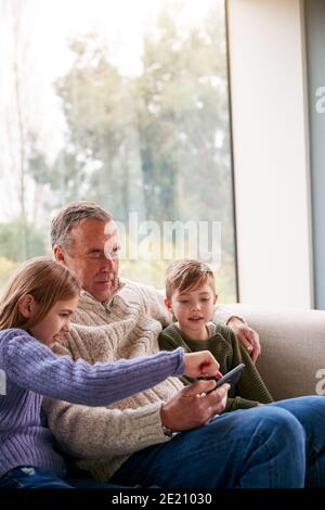 Enkelkinder Auf Sofa Zu Hause Zeigt Großvater Wie Man Benutzt Mobiltelefon Stockfoto