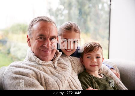 Portrait Von Enkelkindern, Die Zu Hause Mit Großvater Auf Dem Sofa Sitzen Stockfoto