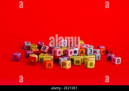 Bunte Holzwürfelperlen mit Buchstaben auf rotem festlichem Hintergrund, Wort "Liebe". Valentinstag. 14 Februar. Flach liegend, Draufsicht. Stockfoto