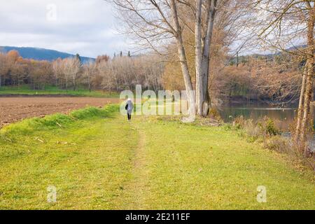 Ein Wanderer geht auf dem Weg entlang, der den Fluss Ter grenzt, wenn er durch Torello geht, an einem bewölkten Wintertag. Stockfoto