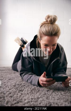 Frau Entspannt Zu Hause Blick Auf Social Media Und Text Nachrichten Auf Dem Mobiltelefon Liegen Auf Dem Teppich Stockfoto