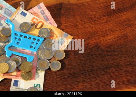 Ein kleiner blauer Einkaufswagen auf Scheinen und Münzen Stockfoto