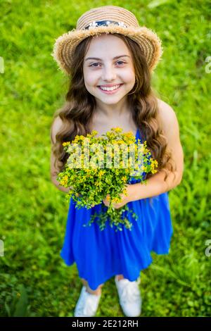 Happy Baby Mädchen tragen Sonnenhut auf lange Weg Haare und Mode Sommerkleid hält Blumen natürliche Landschaft, floral Shop. Stockfoto