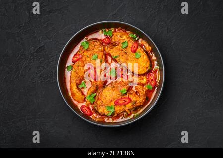 Macher Jhol in schwarzer Schale auf dunkler Schieferplatte. Indische Küche Bengalischer Fisch Curry. Asiatische Speisen und Gerichte. Draufsicht Stockfoto