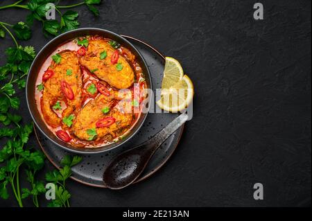 Macher Jhol in schwarzer Schale auf dunkler Schieferplatte. Indische Küche Bengalischer Fisch Curry. Asiatische Speisen und Gerichte. Draufsicht. Speicherplatz kopieren Stockfoto