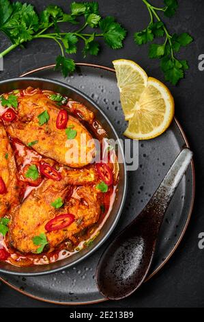 Macher Jhol in schwarzer Schale auf dunkler Schieferplatte. Indische Küche Bengalischer Fisch Curry. Asiatische Speisen und Gerichte. Stockfoto