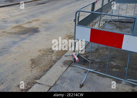 Stahlzaun um die Aushub in der Asphaltstraße. Vor dem Betreten des reparierten Straßenabbaus eine Barriere bauen. Stahlbauzaun mit einem Stockfoto