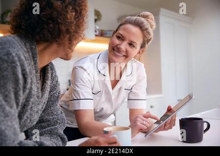 Reife Frau Im Morgenmantel Zu Hause Im Gespräch Mit Weiblich Krankenschwester Mit Digitalem Tablet Stockfoto