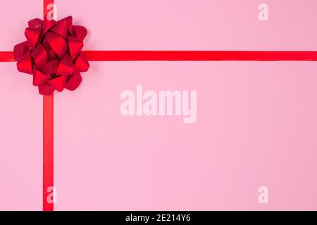 Flache Lay-Komposition mit dekorativer roter Schleife auf rosa Hintergrund mit Platz für Text. Geben präsentiert Konzept. Grußkarte oder Feiertage Stockfoto