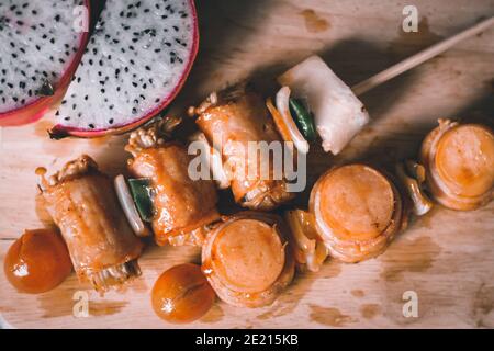 Der Schuss von den Enoki Pilzfleischrollen in den Spiessen auf Ein Holzbrett Stockfoto