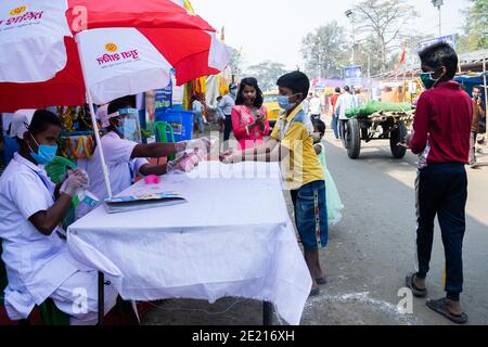 Kolkata, Westbengalen, Indien. Januar 2021. Staatliche Gesundheitsarbeiter sprühen Handdesinfektionsmittel in die Hände der Kinder auf dem Gangasagar-Messegelände. Gangasagar Messe ist eine heilige jährliche Gemeinde von hinduistischen Pilgern. Diese findet auf der Insel Sagar statt, die am Zusammenfluss des Flusses Ganga und der Bucht von Bengalen liegt. Am Tag des "Sakar Sankranti" (14. Januar) nehmen Pilger an diesem Zusammenfluss ein heiliges Bad. Aufgrund der anhaltenden Pandemie-Situation ist das ganze unter starken COVID19-Protokollen eingeschränkt. In diesem Jahr sind die Hauptziele der Regierung die regelmäßige Gesundheitskontrolle, die Desinfektion der pla Stockfoto