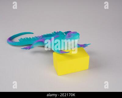Spielzeug-Leguan-Eidechse auf einem grauen und gelben Hintergrund, Konzeptfoto, Platz für Text. Stockfoto