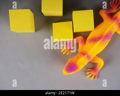 Spielzeug-Leguan-Eidechse auf einem grauen und gelben Hintergrund, Konzeptfoto, Platz für Text. Stockfoto