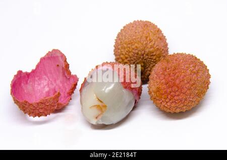 Nahaufnahme einer Gruppe von Litschis, einer tropischen Frucht aus Asien, isoliert auf weißem Hintergrund. Eine ist teilweise geschält und zeigt darunter milchig weißes Fleisch. Stockfoto