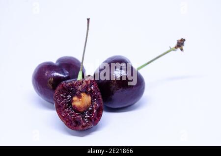 Drei Kirschen isoliert vor einem weißen Hintergrund, eine wurde in der Hälfte gebissen zeigt das saftige Fleisch und Samen im Inneren. Stockfoto