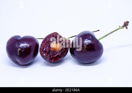 Drei Kirschen in einer Linie, isoliert vor weißem Hintergrund. Die mittlere Kirsche hat einen Bissen herausgenommen, der den Stein und das Fleisch im Inneren zeigt. Stockfoto