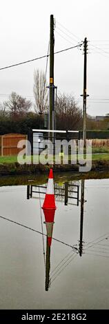 Kegel auf dem Eis, Wasser des Kanals war gefroren, ein Verkehrskegel sitzt auf dem Eis mit elektrischen Drahtstangen aufgereiht verursacht eine vertikale Reflexion Stockfoto