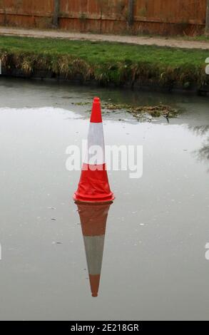 Kegel auf dem Eis, das Wasser des Kanals war gefroren und jemand hat einen Verkehrskegel auf dem Eis in der Nähe von gefrorenem Unkraut positioniert. Stockfoto