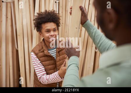 Hochwinkel-Porträt des lächelnden afroamerikanischen Jungen Einkaufen mit Vater Im Baumarkt hilft bei der Auswahl von Holzbrettern für den Bau Oder zu Hause Stockfoto