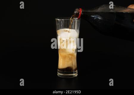 Gießen Sie die Cola aus einer Plastikflasche in ein Glas Eis auf schwarzem Hintergrund-Lebensmittel-und Getränke-Konzepte. Stockfoto