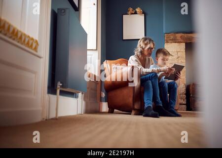 Enkel Mit Großmutter Sitzt Im Stuhl Spielen Auf Digital Tablet Gemeinsam Zu Hause Stockfoto
