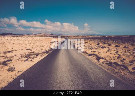 Lange gerade Asphaltstraße mit Sand und Felsen Wüste herum - Reise und Destination Abenteuer Konzept - schöne Landschaft und Blauer Himmel mit Wolken Stockfoto