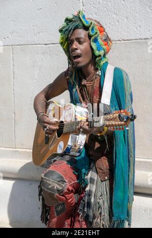 Ein Straßenmusikant in einem bunten Hut & Outfit spielen & singen auf der Gitarre im Washington Square Park in New York City Stockfoto