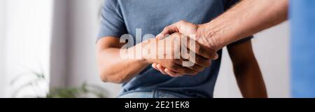 Beschnittene Ansicht von multikulturellen Männern, die in der Klinik die Hände schütteln, Banner Stockfoto