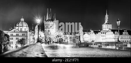 Spaziergang auf der Karlsbrücke, Tschechisch: Karluv Most, bei Nacht. Beleuchtete Statuen und Altstädter Brückenturm. Prag, Tschechische Republik. Schwarzweiß-Bild. Stockfoto