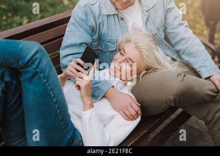 Draufsicht auf ziemlich blonde Frau ist mit Smartphone, mit Ruhe mit ihrem Mann auf einer Gassenbank. Romantisches Date Stockfoto