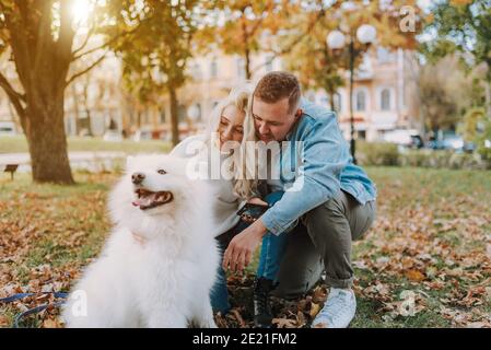 Glücklicher junger Mann und Frau genießen von Spaziergang mit flauschigen Samoyed Hund mit Herbstlandschaft im Hintergrund Stockfoto