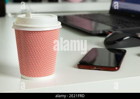 Büroarbeitsplatz Schreibtisch mit Coffee to go Tasse, Telefon und Laptop auf verschwommenem Hintergrund Stockfoto