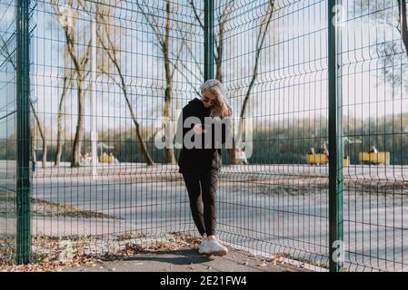 Volle Länge der schönen Frau hält Smartphone während des Stehens auf Basketballplatz im Freien Stockfoto