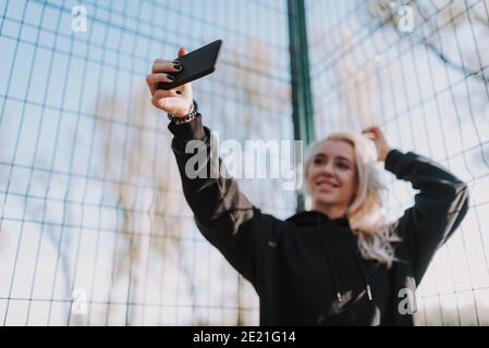 Portrait der glücklichen schönen Dame mit Handy während der Herstellung Foto auf Basketballplatz Stockfoto