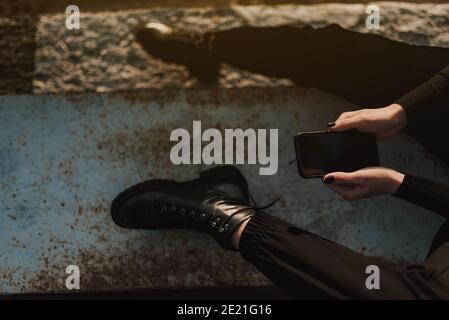 Draufsicht der jungen Frau in schwarz tragen und Stiefel Mobiltelefon im Freien verwenden Stockfoto