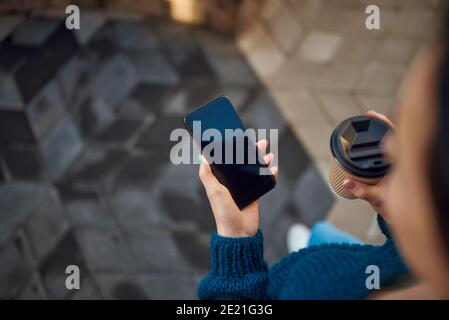 Draufsicht auf junge Dame hält Smartphone und Papiertasse Beim Spaziergang in der Stadt Stockfoto