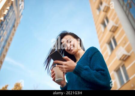 Liebenswert junge Brünette mit fließenden Haar SMS von Smartphone während Ihre Promenade im Stadtzentrum Stockfoto