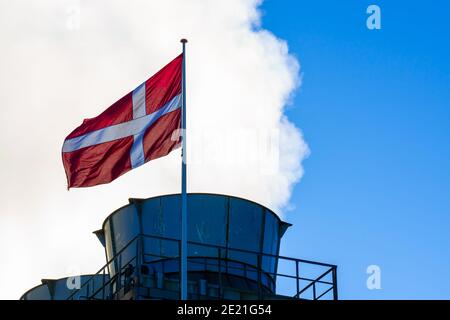 Schornstein mit Dampf und Rauch und einer dänischen Flagge im Vordergrund. Stockfoto