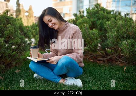 Liebenswert junge Dame genießen einen spannenden Roman und verbringen Zeit Mit ihm im Freien auf einem grünen Rasen Stockfoto