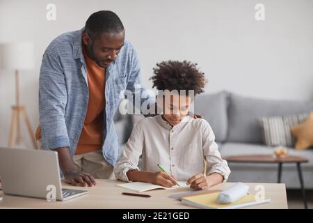 Porträt des stolzen afroamerikanischen Vaters, der Teenagerjungen hilft, Hausaufgaben am Schreibtisch zu machen, in moderner Wohneinrichtung, Kopierraum Stockfoto