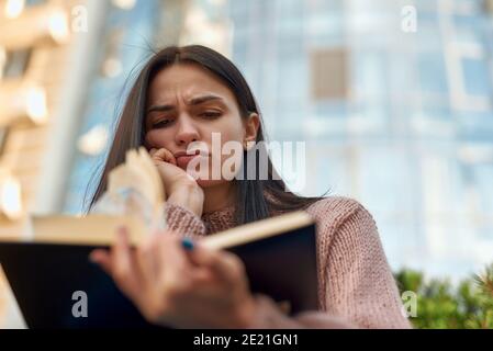 Aufgeregt und verzweifelt weibliche Brünette liest Buch in der Stadt Straße Stockfoto