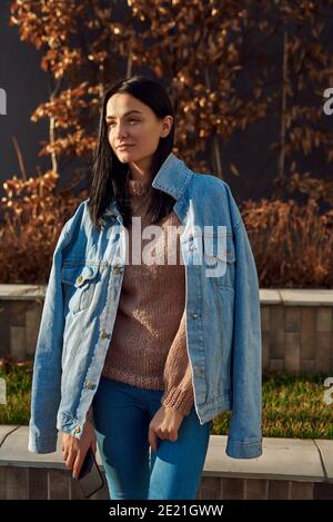 Ruhige und positive junge Frau, die in einer entspannten Pose steht In der gemütlichen Gasse eines ruhigen Stadtplatzes Stockfoto