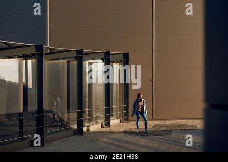 Hübsche Frau in Jeans, Jeansjacke, Strickpullover und Sneakers, die auf modernem urbanen Hintergrund posieren Stockfoto