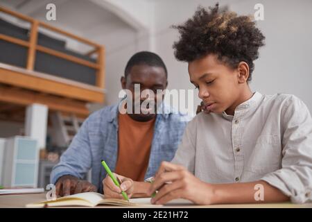 Porträt eines afroamerikanischen Jungen im Teenageralter, der Hausaufgaben macht oder bei dem er studiert Zuhause, während er am Schreibtisch saß und Vater ihm half Stockfoto