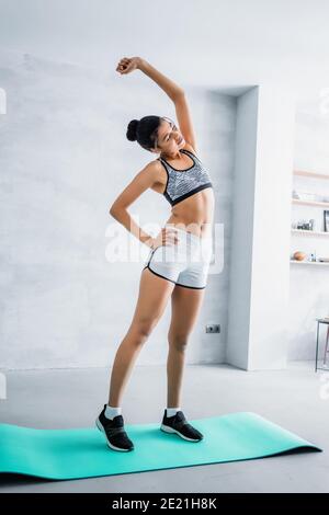 In voller Länge Ansicht von afroamerikanischen Frau in Sportswear tun Side-Bend-Übung auf Fitnessmatte zu Hause Stockfoto