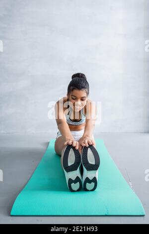 Lächelnd afroamerikanische Sportlerin tut sitzend vorwärts beugen Übung an Zu Hause Stockfoto