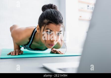 afroamerikanische Sportlerin tut Liegestütze Übung in der Nähe Laptop auf Verschwommener Vordergrund Stockfoto