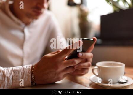 Zugeschnittenes Foto eines jungen Mannes in weißem Hemd, der auf dem Smartphone tippt, während er sich im Café ausruhte. Lifestyle-Konzept Stockfoto